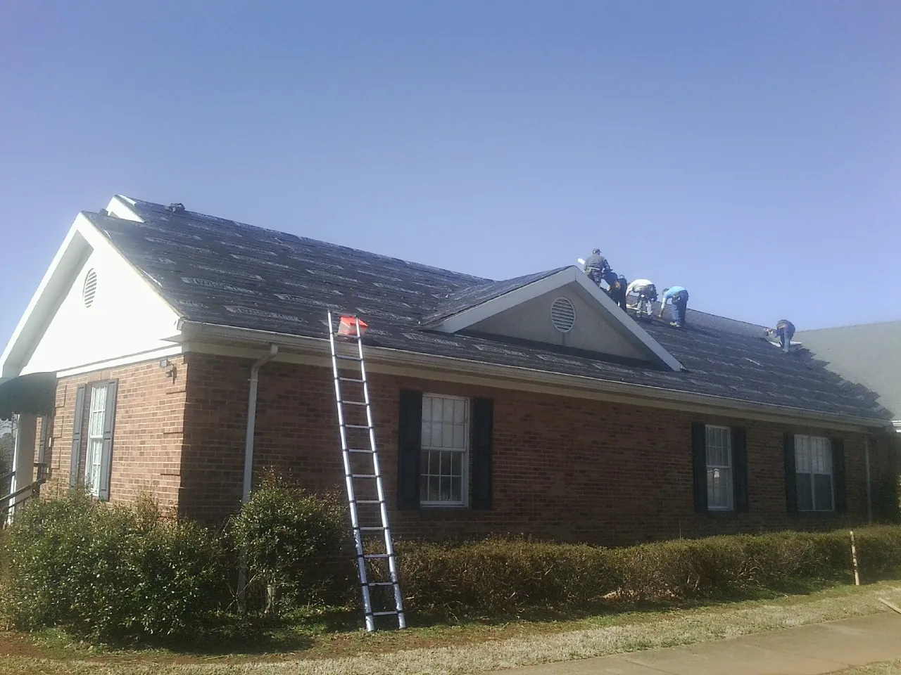 Crew tearing shingles off a brick ranch roof with a ladder set — Emergency Roof Repair work by our crew in Scotts