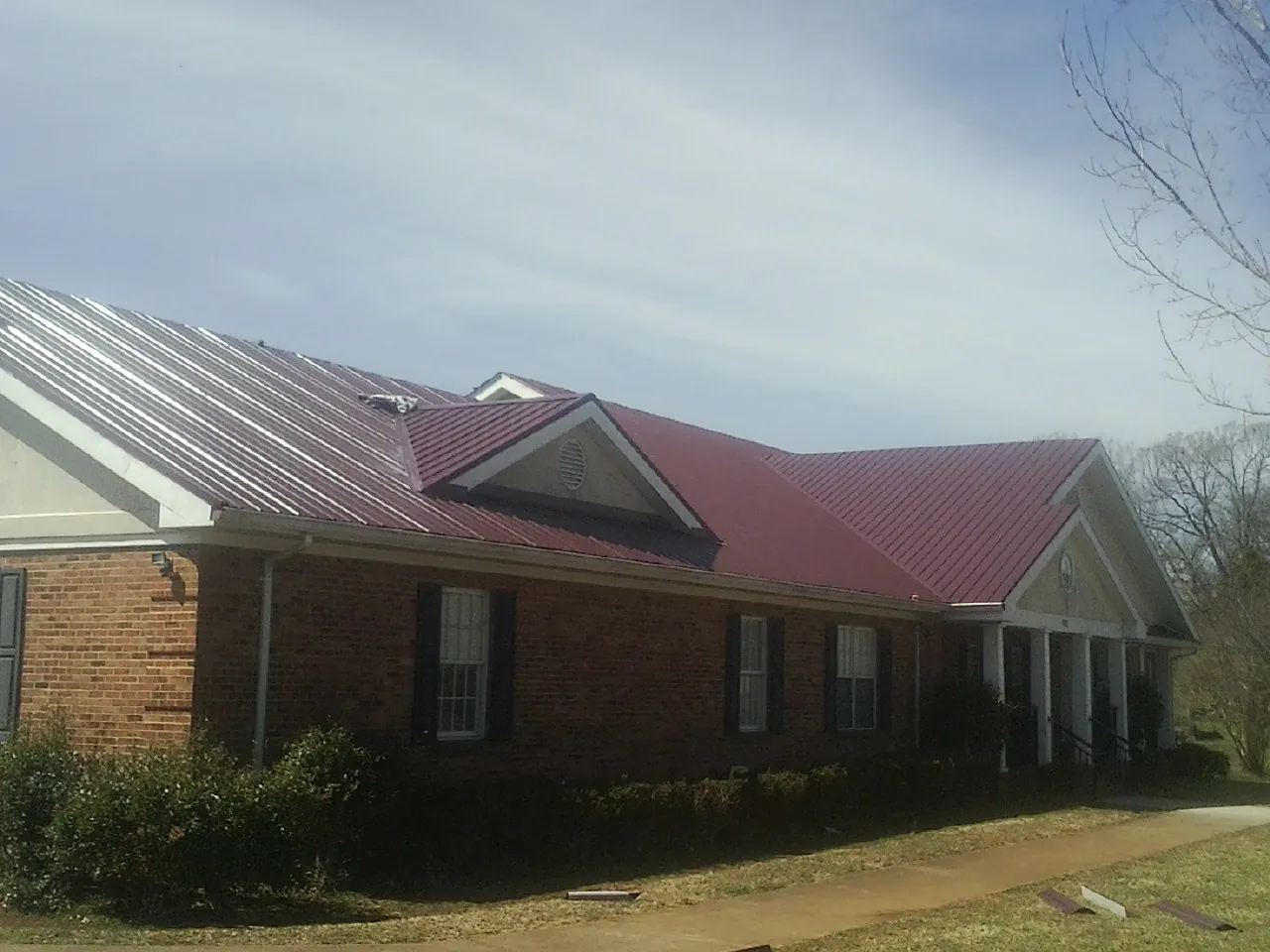Red metal roof with gabled entries on a long brick building, from a Hail Damage Roof Repair job in Scotts