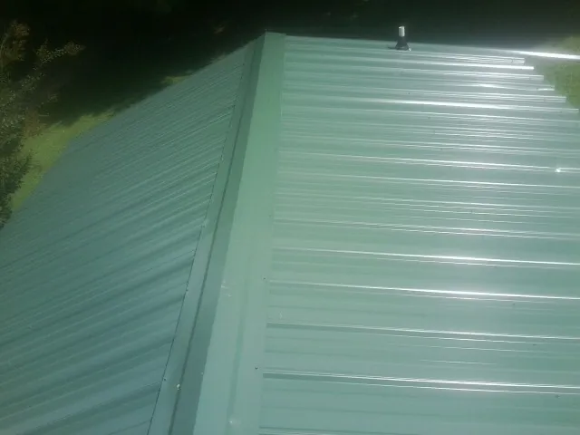 New green metal panels meeting at the ridge of a roof — Flat Roof Repair work by our crew in Scotts
