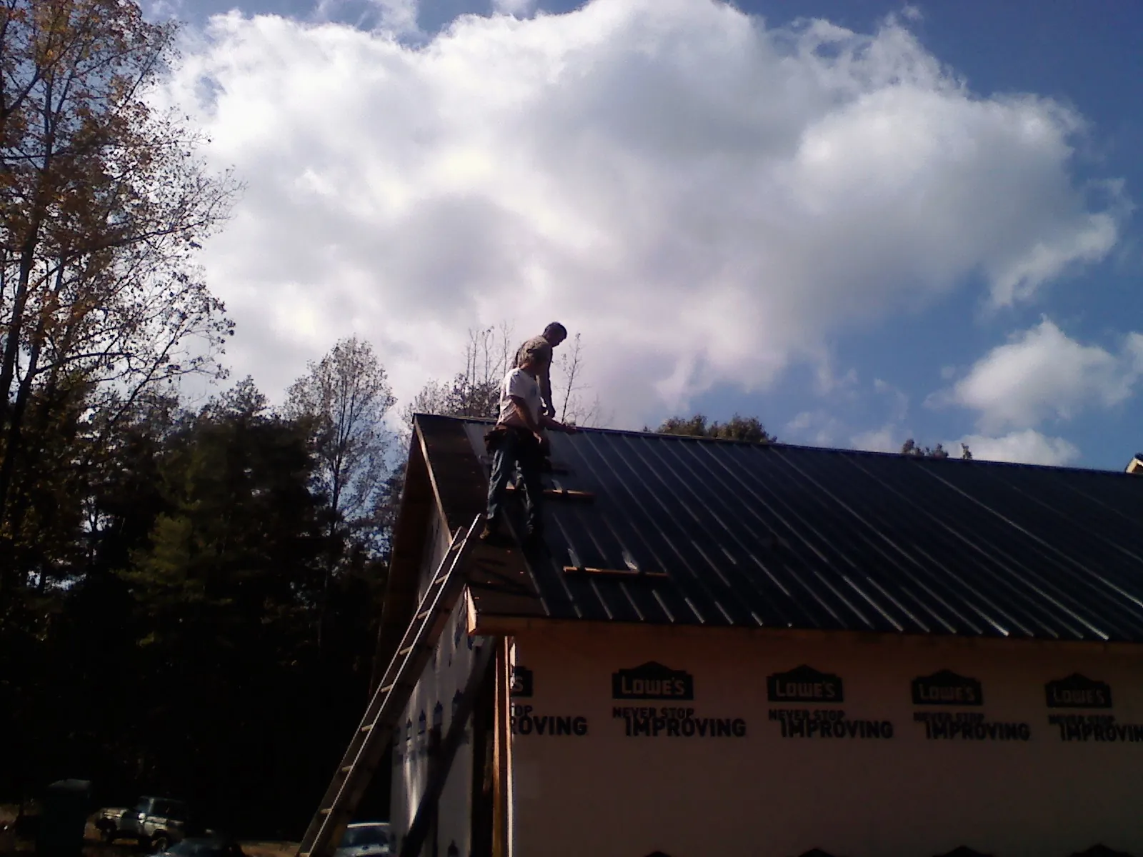 Roofer fastening dark metal panels high against a cloudy sky, from a Roof Inspection job in Scotts