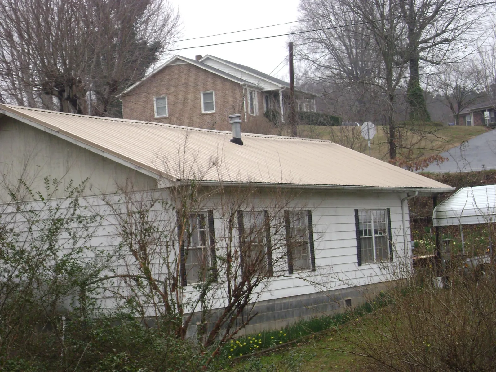 Tan metal roof on a white sided house set into a hillside — Commercial Roofing by Roofing Brothers in Scotts